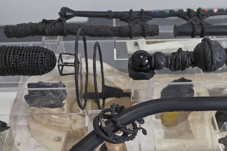 Detailed image of sculptures resting on plexiglass vitrine, depicting objects bound with wire and rope, spheres, geometries. 