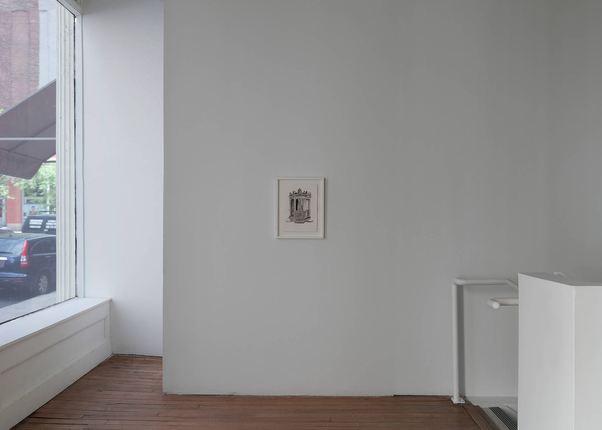 A small black ink drawing of a confession booth in white frame hangs in a dark gallery.