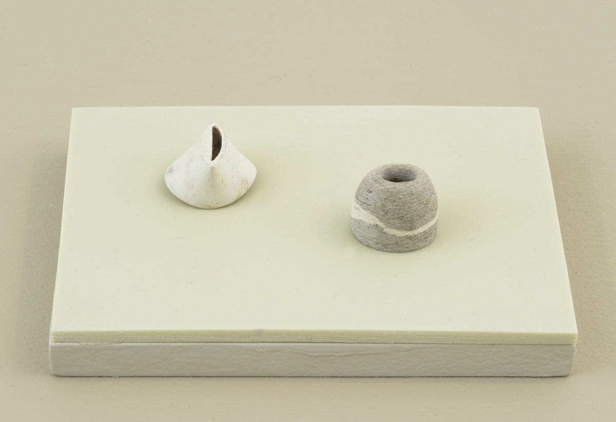 Two abstract, miniature sculptures resembling objects found in nature placed on top of a green-tinted plinth. 