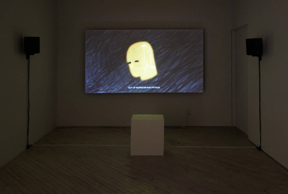 Installation image of a video room with two speakers to left and right and a color 6:9 image at center, at bottom a white cube seat. The video image is from a hand drawn animation. Dark grey background with grey and black sketchy marks of pencil, at center is the yellow silouhette with black eyes of a man's head in 3/4 profile. At bottom is a subtitle which reads, "OUT OF BOREDOM AND FATIGUE".