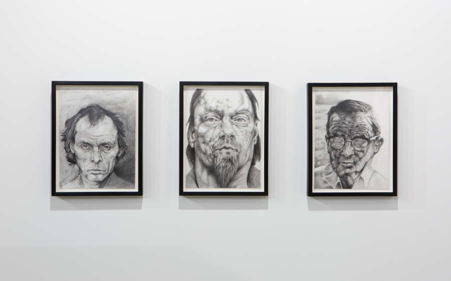 Three framed graphite drawings hung in a row depicting close of images of three older men.
