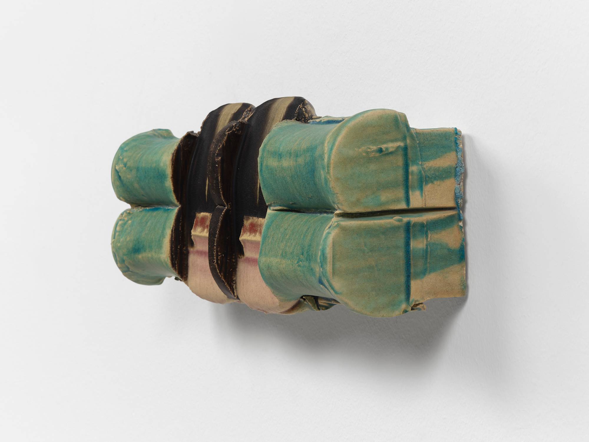 Three quarter view of a symmetrical ceramic sculpture composed of two horizontally stacked cylinders that have been perpendicularly stamped twice towards the center and glazed in hues of aqua, pink, brown, and red.