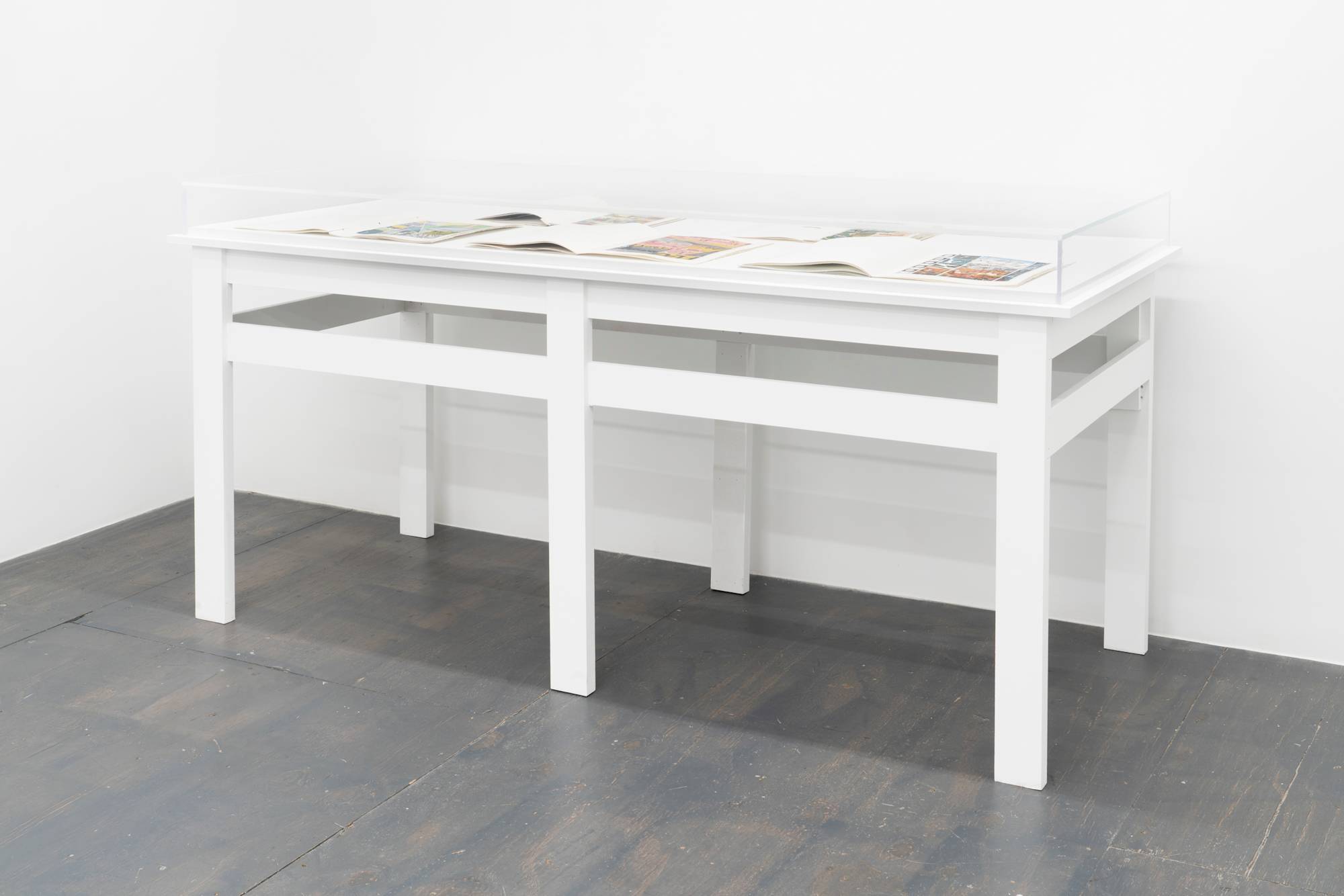 A large vitrine placed facing a gallery wall containing multiple artist books spread open.