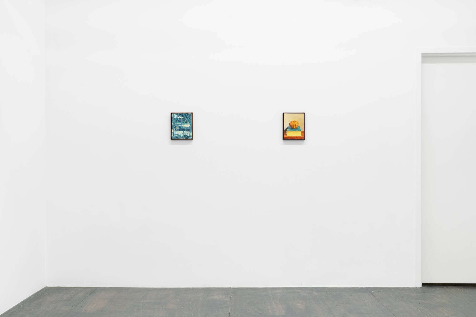Two small framed paintings are displayed in a line on a plain white wall next to a door with a grey painted wood floor below. The artworks depict various scenes, including elevated train tracks and a squash sitting on a book.