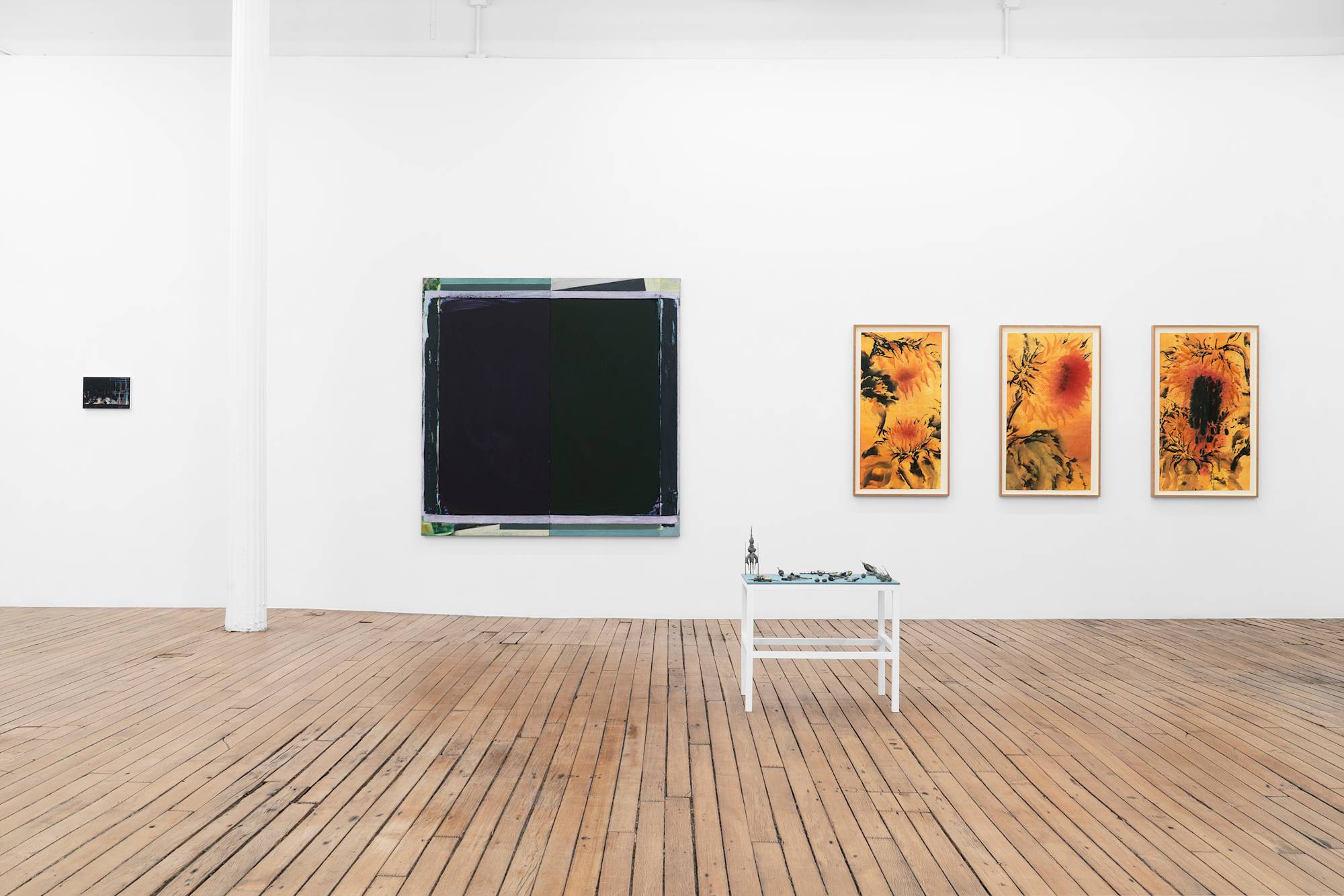 An art gallery displays a collection of paintings and a small, simple table with blue fabric top and sculptural elements.