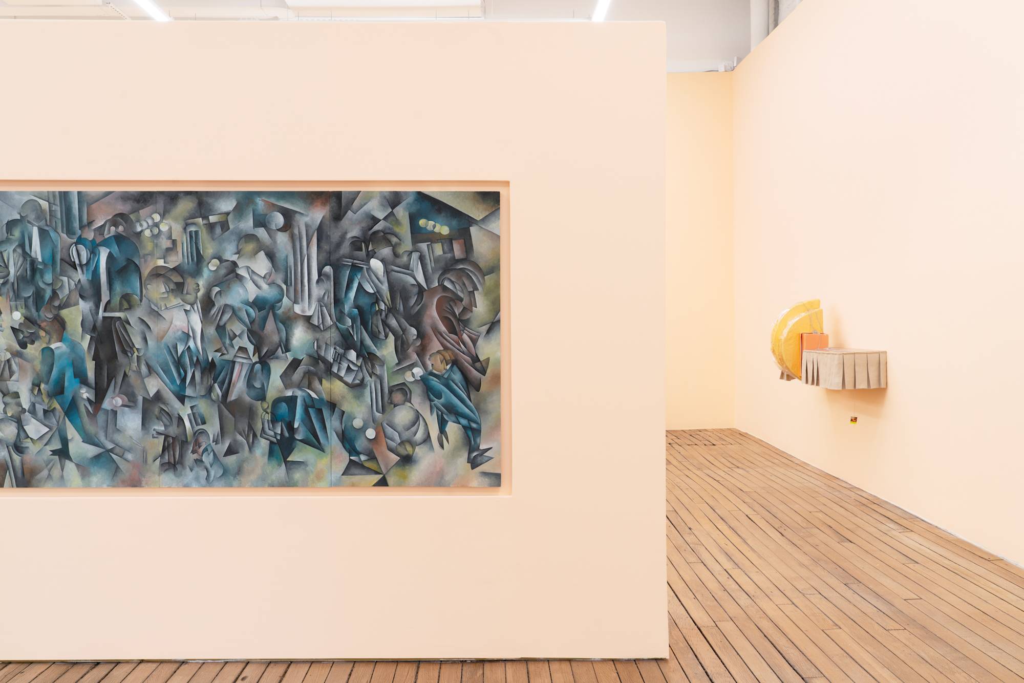 Interior view of art gallery with wood floors and peach colored walls. Various sculptures hang on the walls.