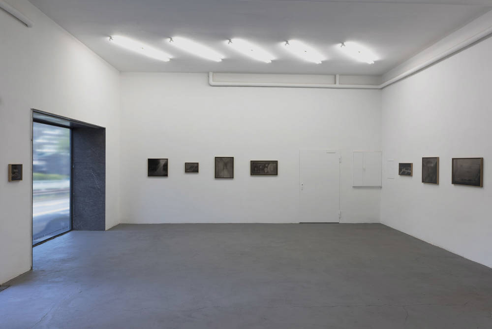 Several framed charcoal drawings in a gallery space with a large window. 