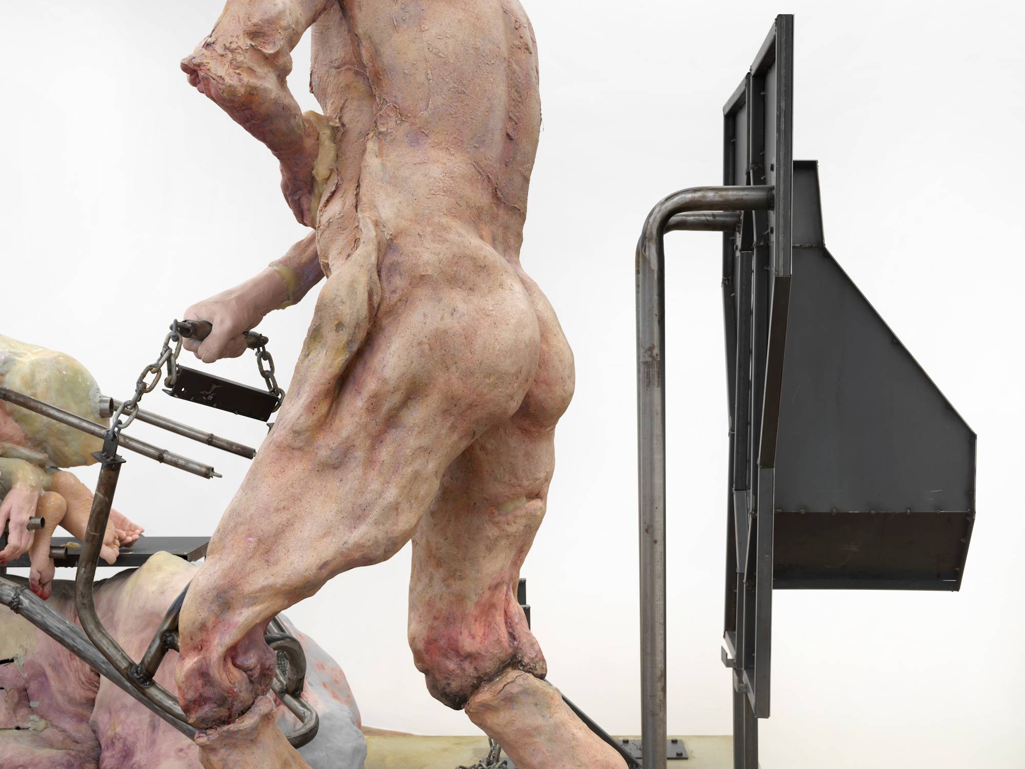 Detail of a large sculpture depicting an abstracted naked body of a man with a steel structure behind him.