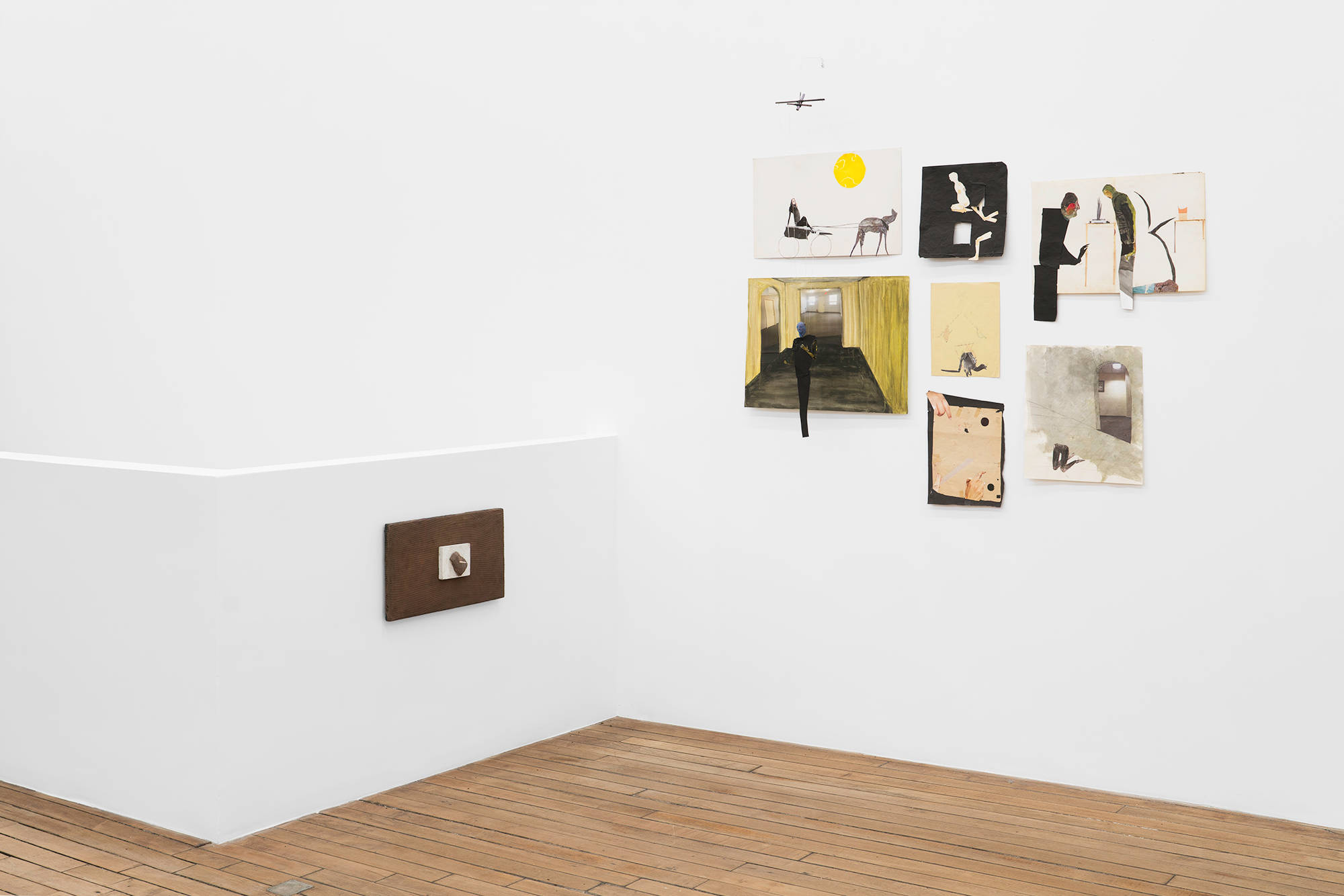 On a guard wall that surrounds the staircase leading to the basement sits a brown painting. On the wall perpendicular to the brown painting is a group of collaged artworks on paper.