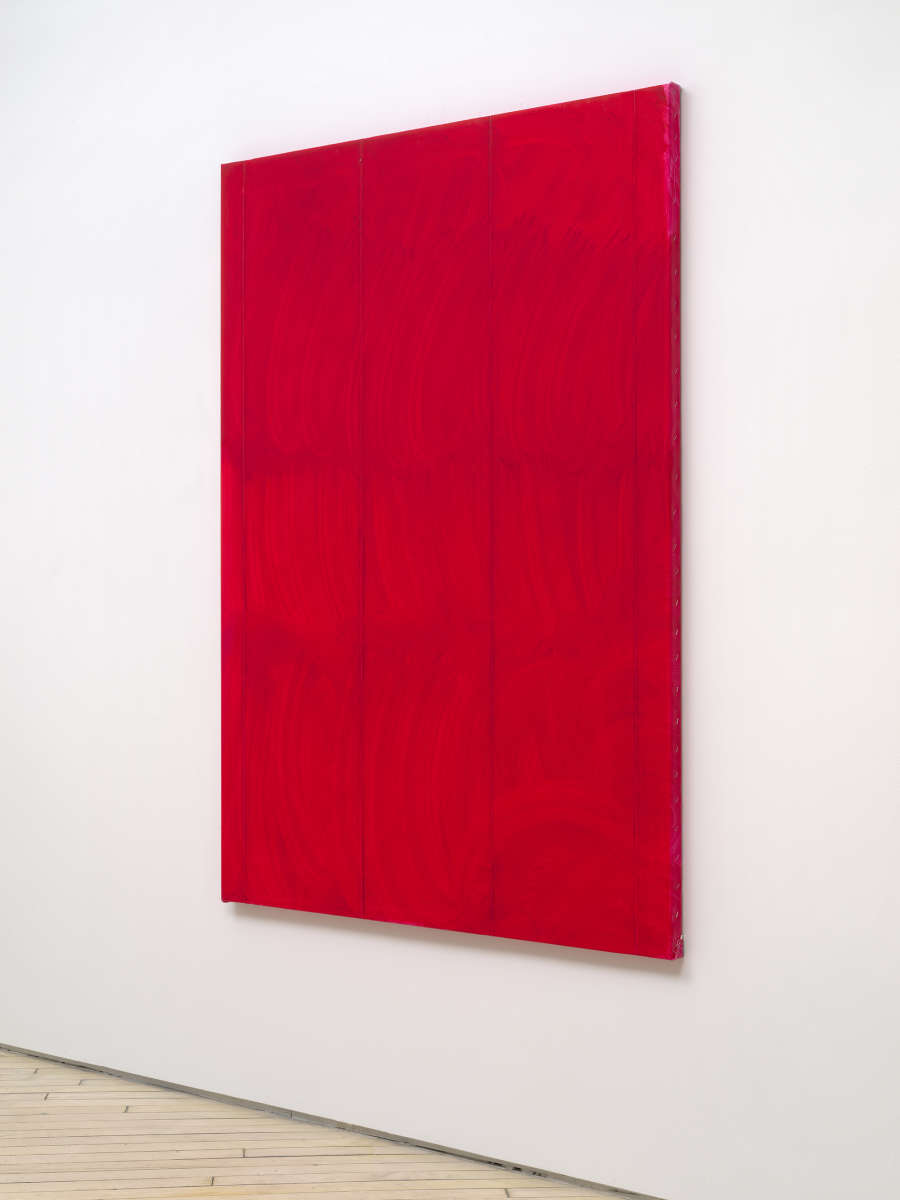 A side view of a large vertical painting. The painting is a red monochrome. The surface is brushy. 