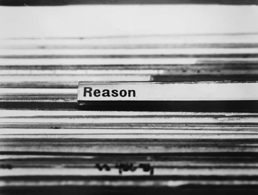 A black and white horizontal photograph with a white background and horizontal black lines of the edges of index cards in a card cagalogue file drawer, and at center, on a tab sticking out of the cards, the type written phrase, 'Reason.' 