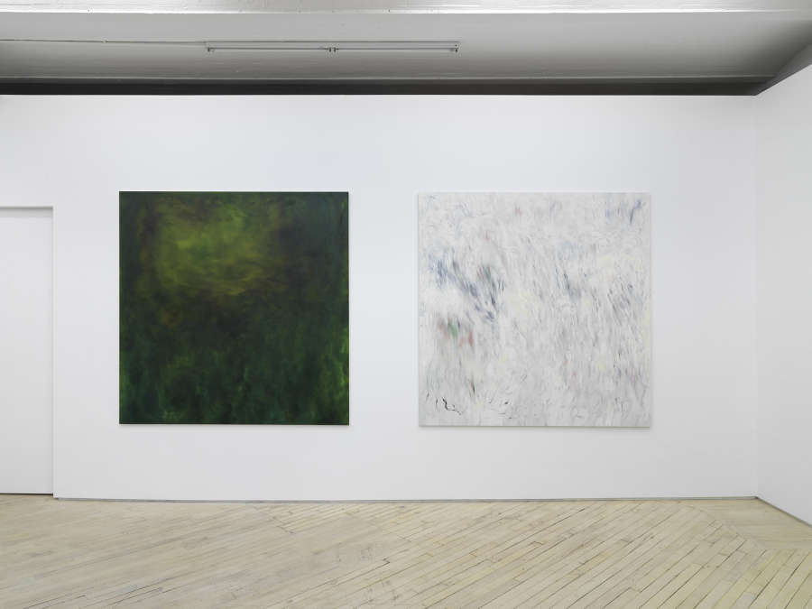 Two large square abstract paintings hung close together on a long gallery wall with a closed door way to the left. 