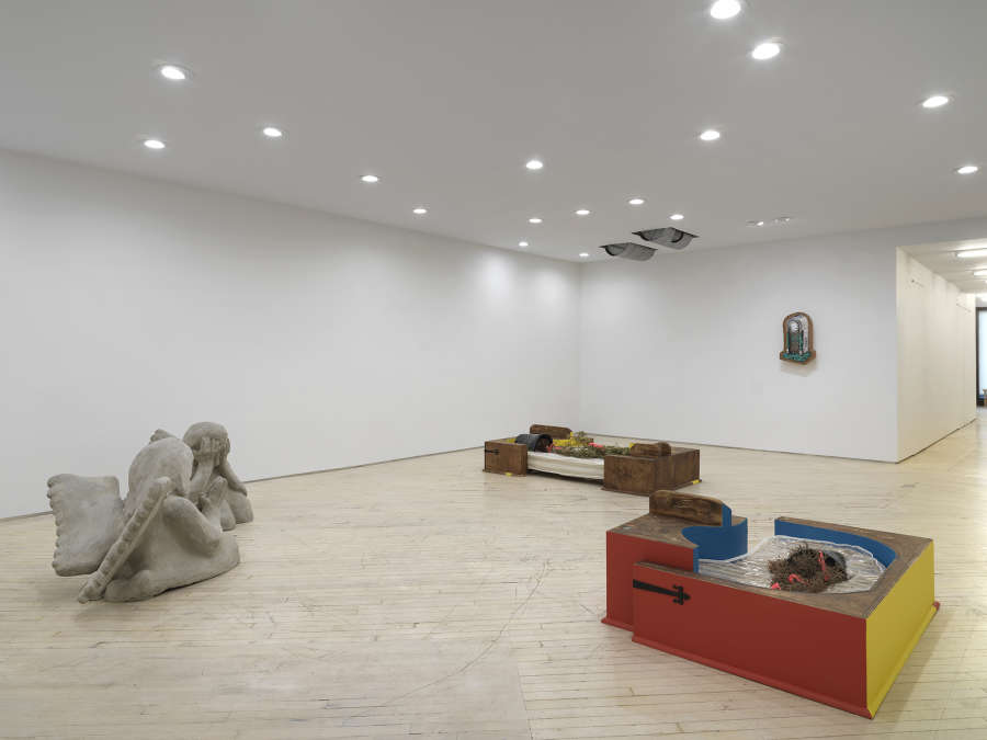Image of a solo exhibition by Libby Rothfeld showing a number of sculptures on the ground and a painting of a clock hanging on the rear wall with two metal drums protruding from the ceiling.