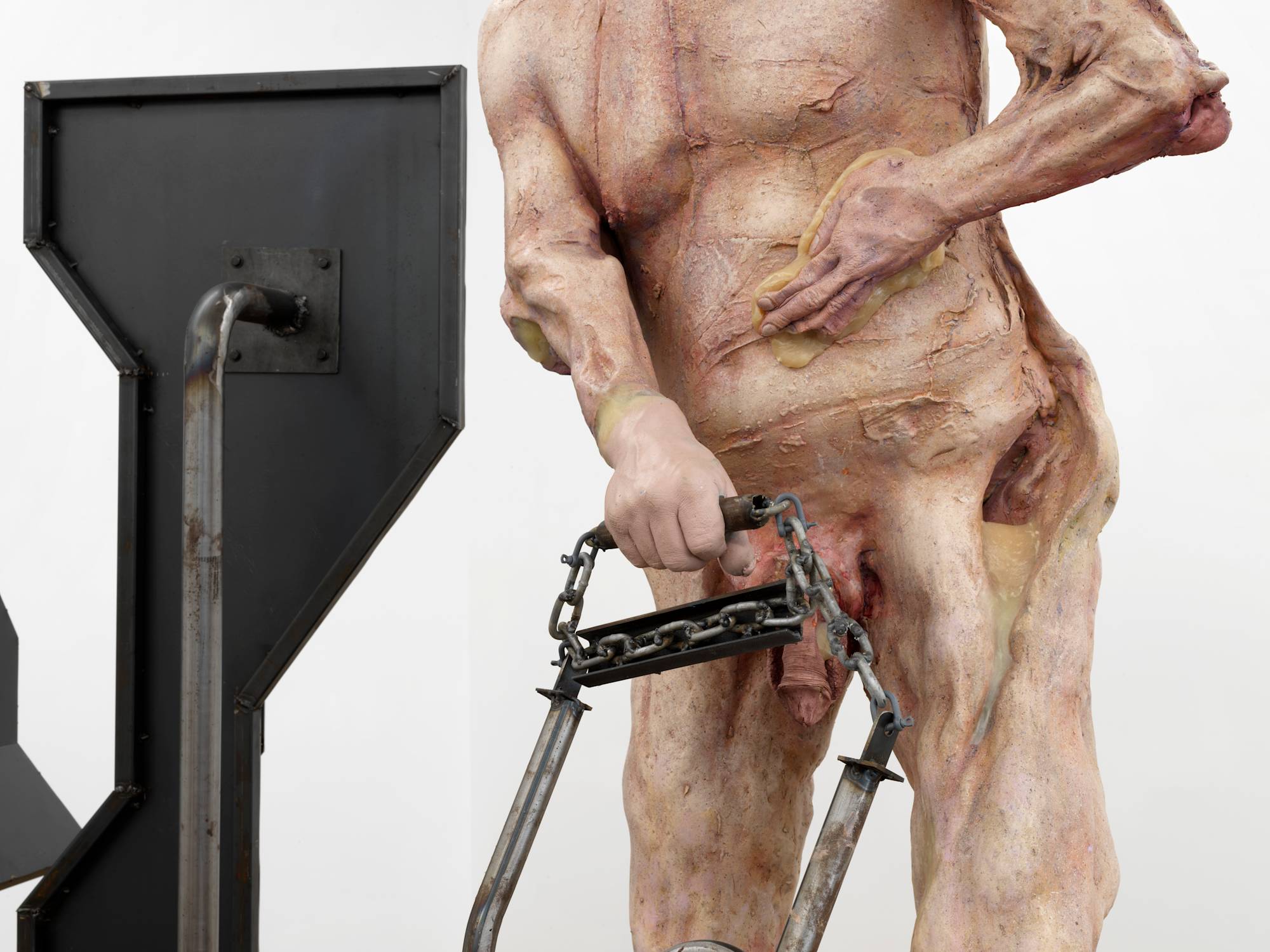 Detail of a large sculpture depicting an abstracted naked body of a man with a steel structure behind him.
