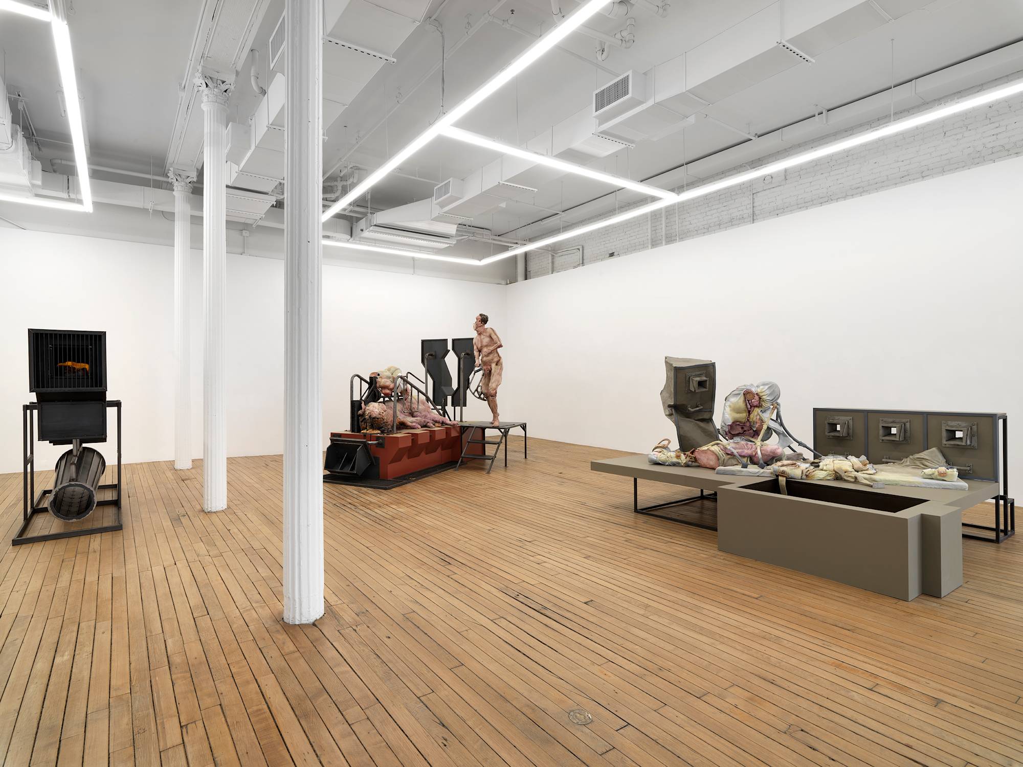 A large gallery space filled with three monumental sculptures. A figure and giant pig rest on top of a platform in the back, a large steel structure on the left.