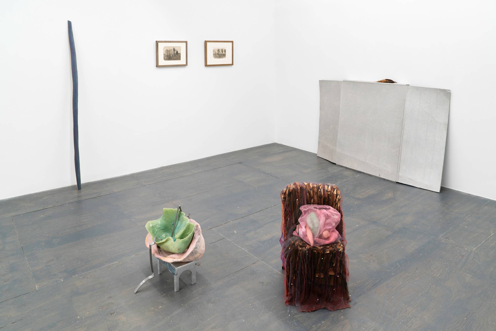View of a group show in the downstairs space of a gallery with white walls and grey floor. There is a mix of framed drawings and sculptural work.