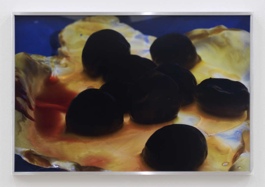 A group of water chestnuts, mostly in shadow and almost completely black, sit on a flat torn object that is covered in a sticky looking orange liquid.