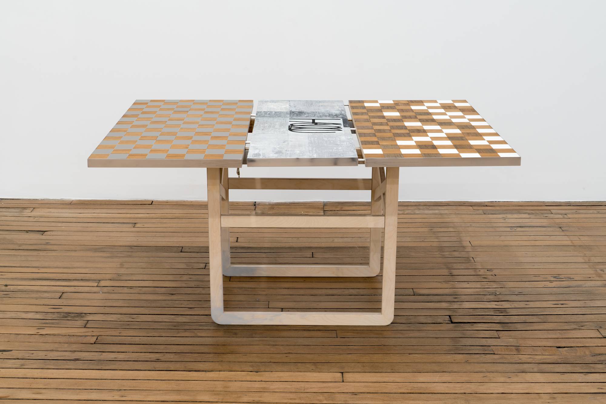 Ian Miyamura plywood table sculpture featuring a checkerboard top and removable leaf painting of depicting the letters "T, A, S, T, E" arranged at different sizes and angles on a light grey background.