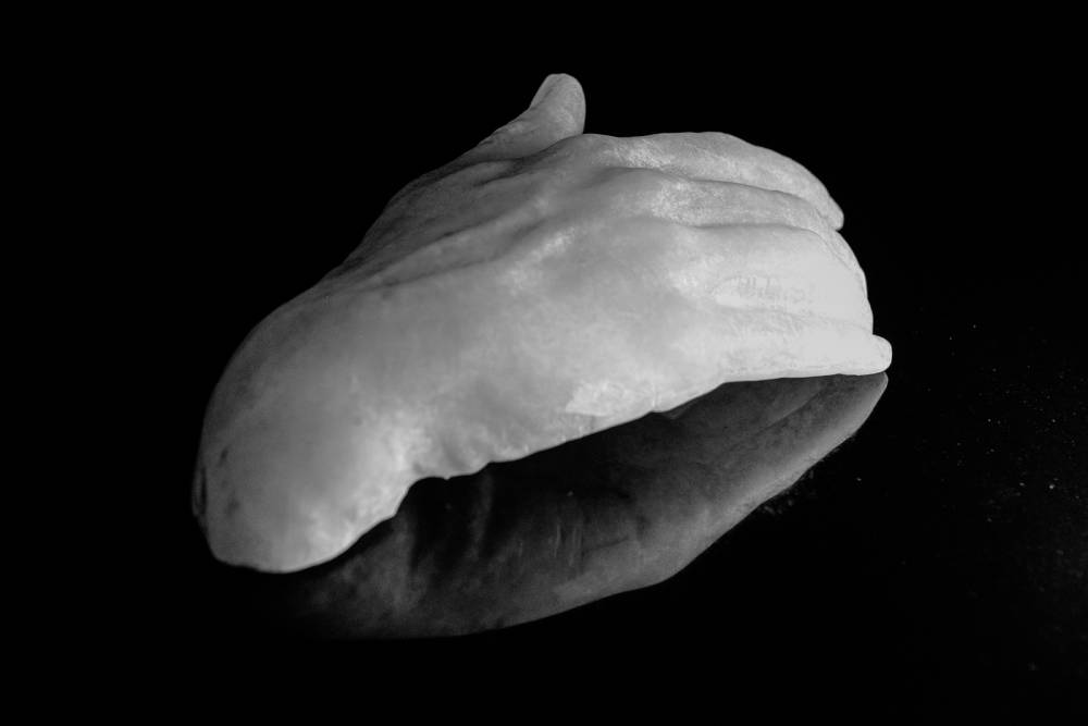 Image of a sculpted hand made from white alabaster sitting on a black reflective surface