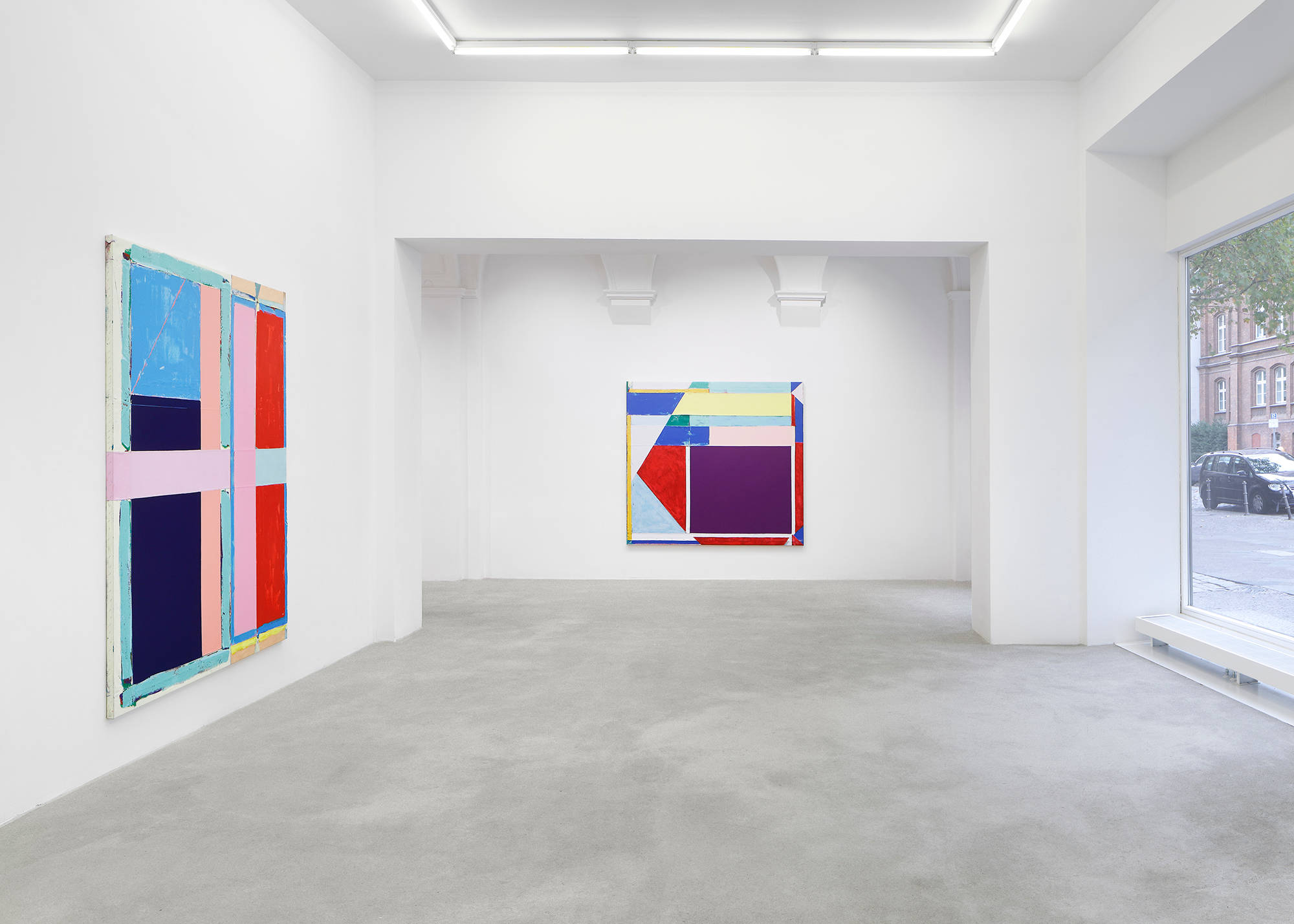 In a gallery space, two large abstract paintings hung on separate walls. The paintings are formally dominated by large rectangular blocks of color. The most striking colors in both paintings are a range of reds, pinks, blues, and yellows. The paint is thick and the canvases are rough.