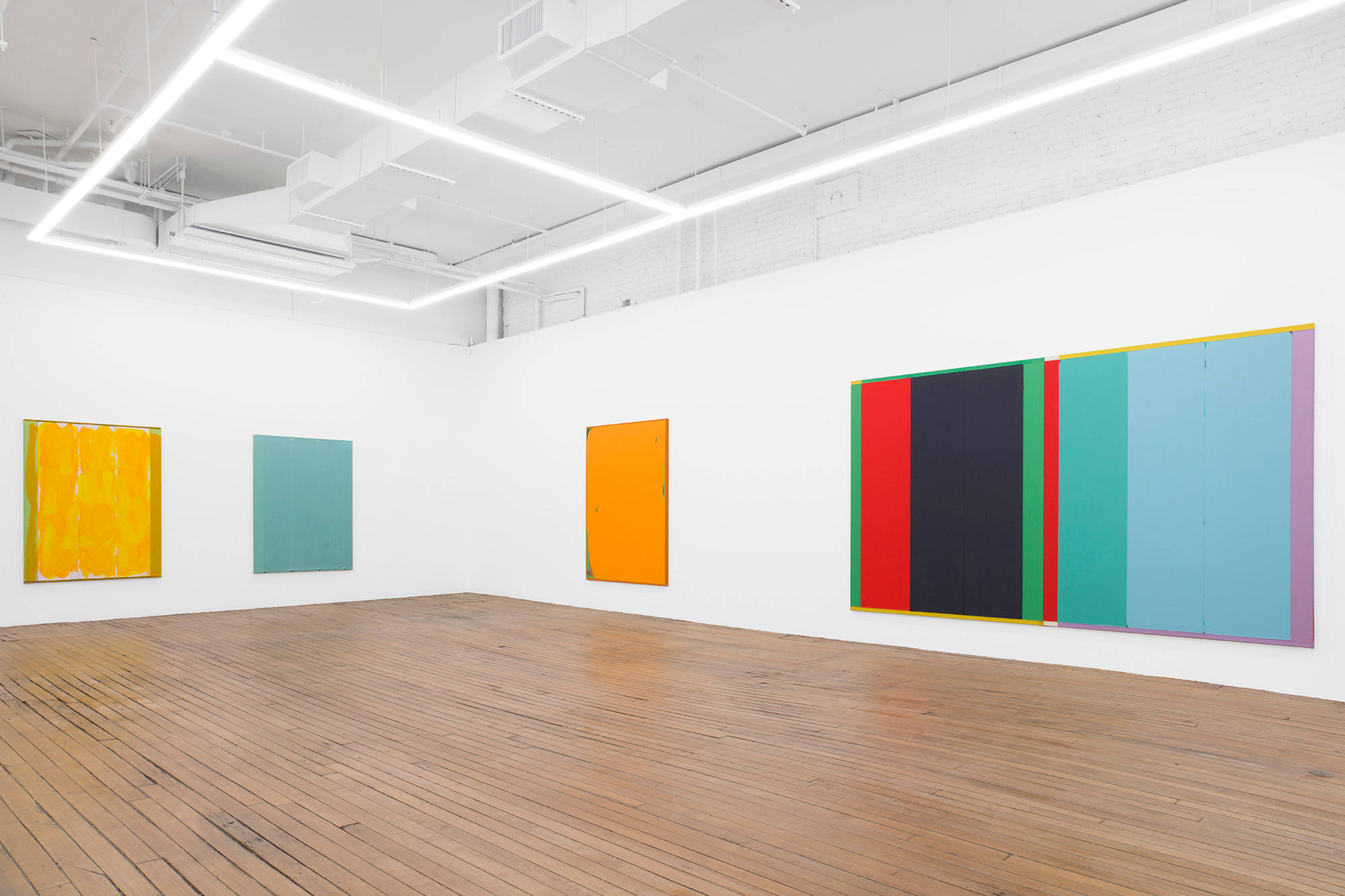 A succession of large, primarily monochromatic abstract paintings hung in a line. The farthest painting to the left is the largest and contains stripes of many different colors.
