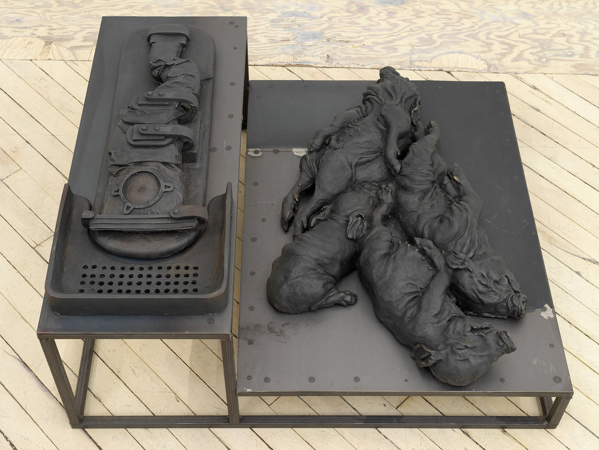 In a gallery space, an iron sculpture depicting abstracted animal forms on top of a plinth.