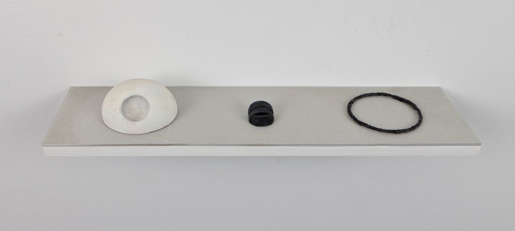 In a gallery space, a shelf is installed at the center of a wall, housing three handmade objects.
