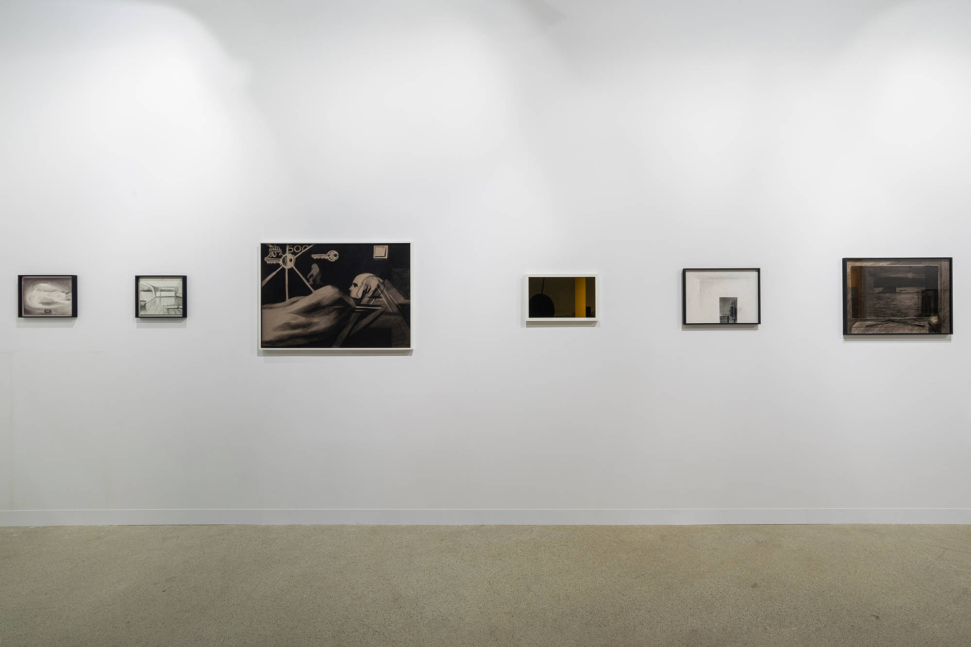 Installation view of an art fair booth front wall, framed drawings hung in a row across the wall.