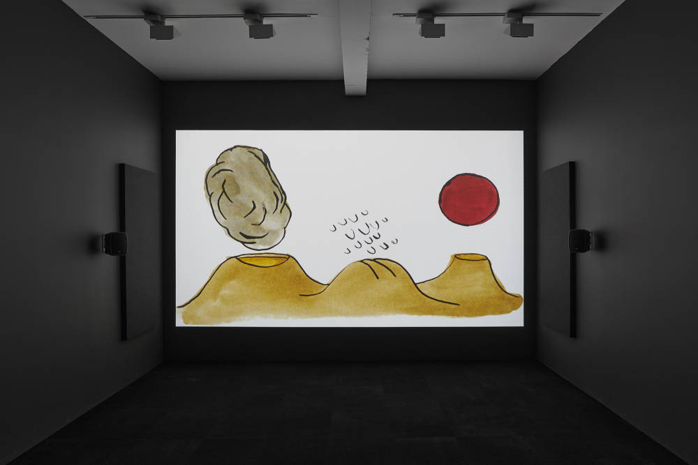 A film is projected in a dark room, the screen bright white with an ink drawing of mountains and volcanoes with a red round sun.