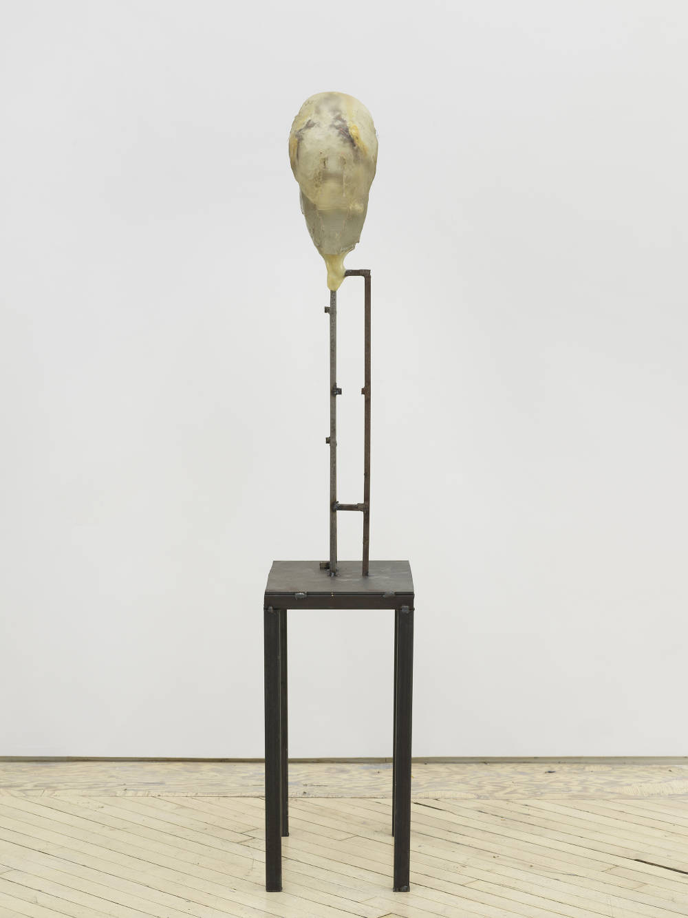 In a gallery space, an abstract sculpture resembling a human form with a steal base. 