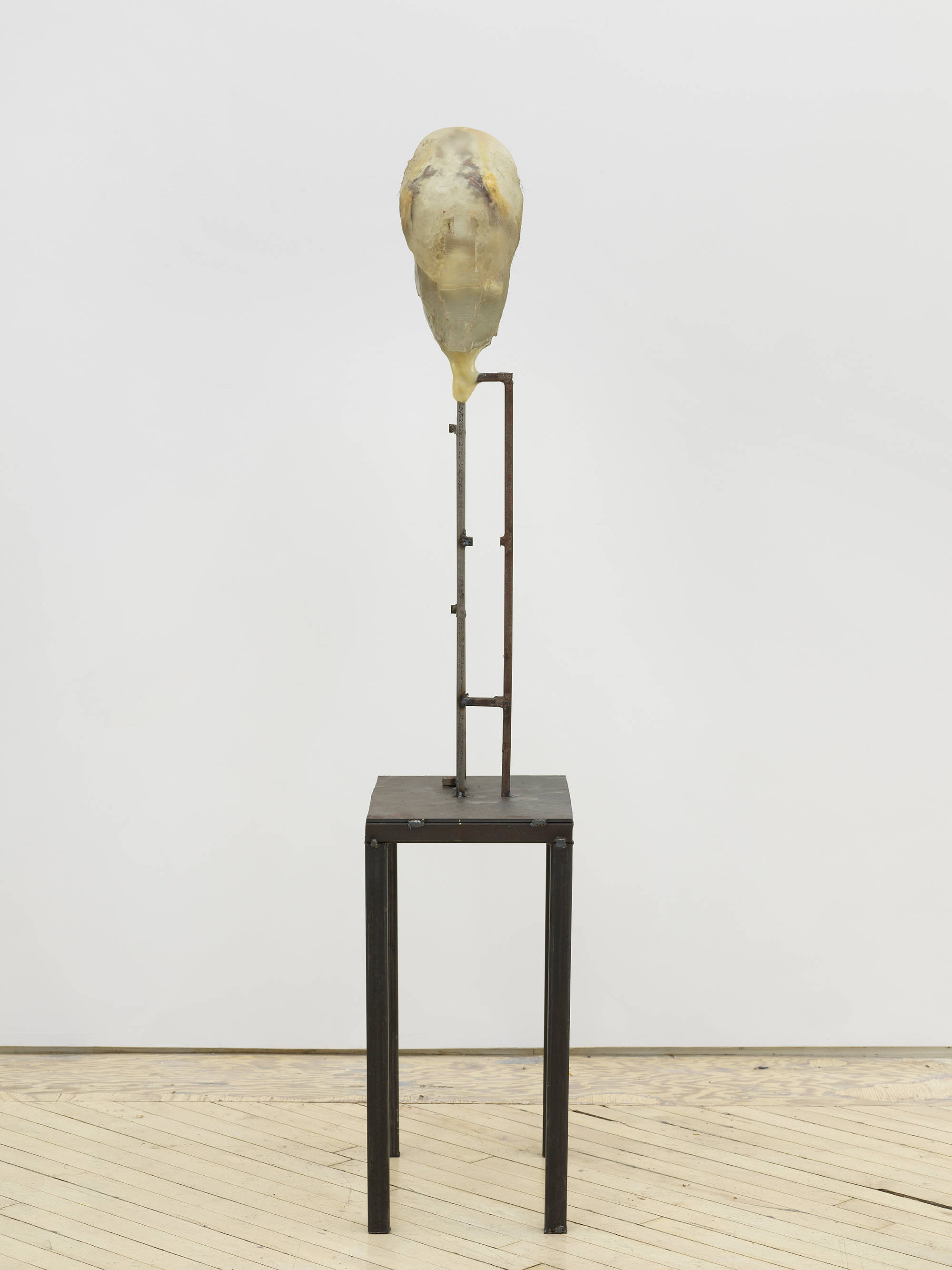 In a gallery space, an abstract sculpture resembling a human form with a steal base.