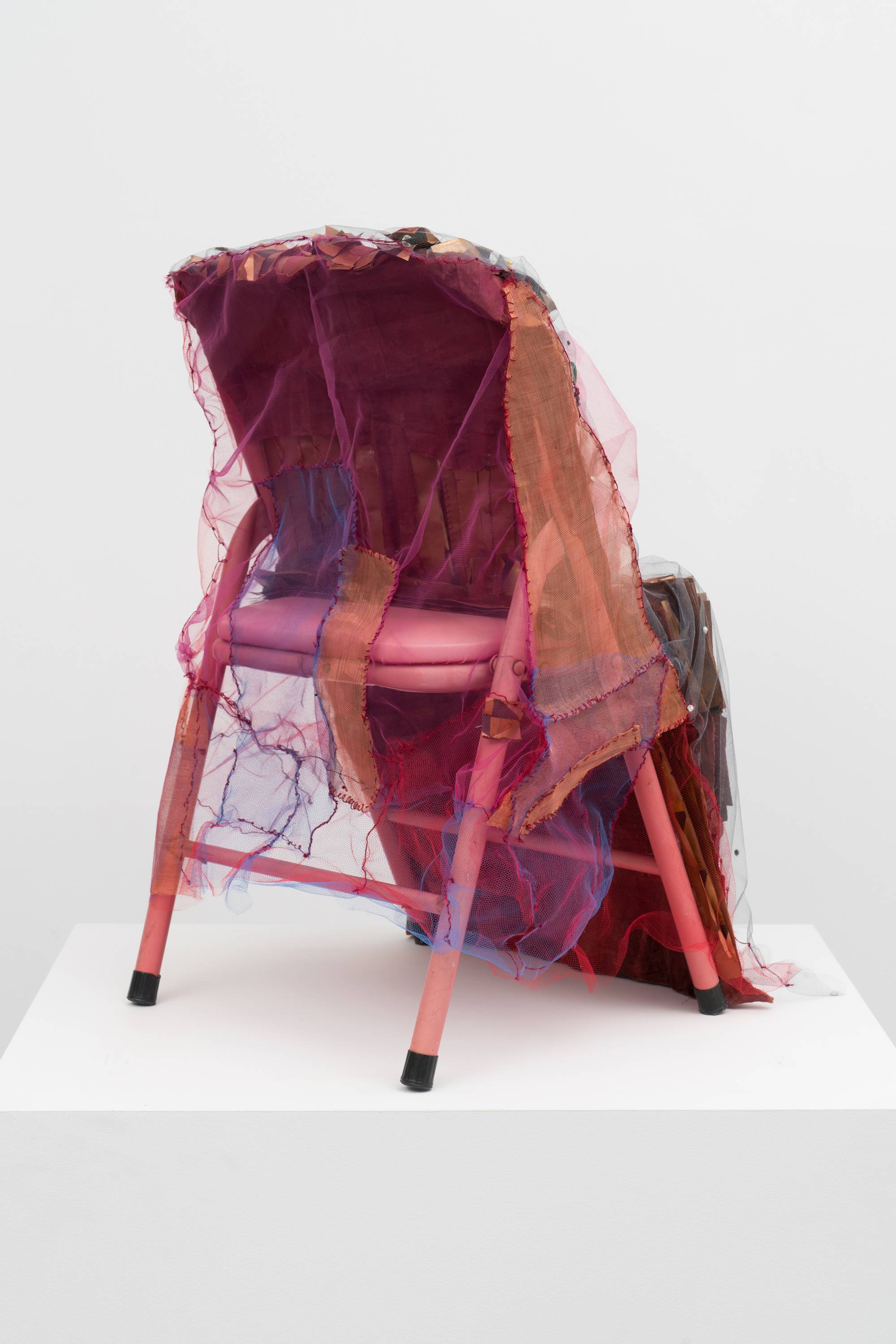 Back view of Em Rooney sculpture of a red children's folding chair adorned with mesh, folded paper, and resin-cast fruit.