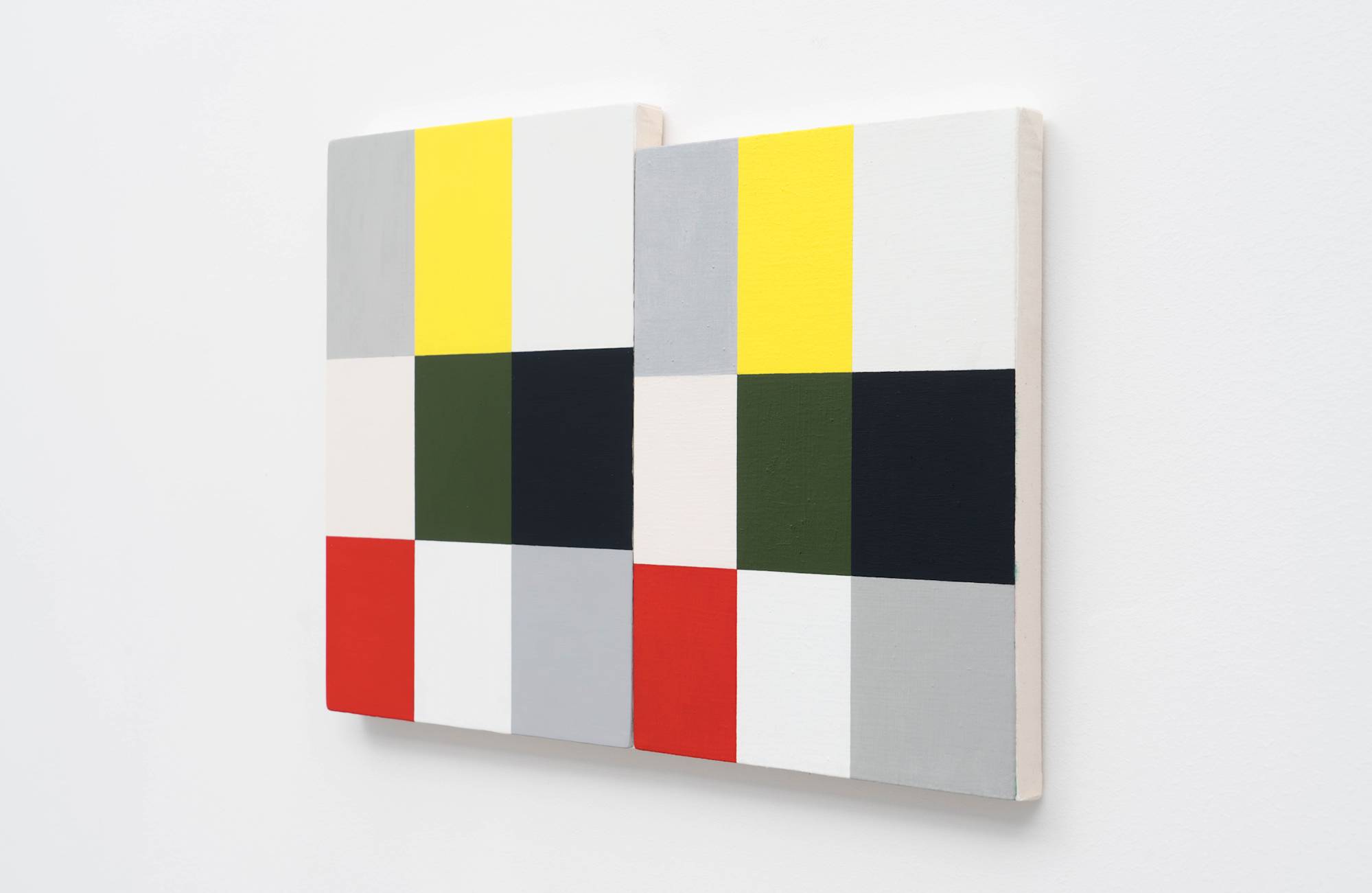 3/4 view of two Ian Miyamura paintings of red, green, black, white, yellow, grey, and pink squares hang on the wall butting against each other.