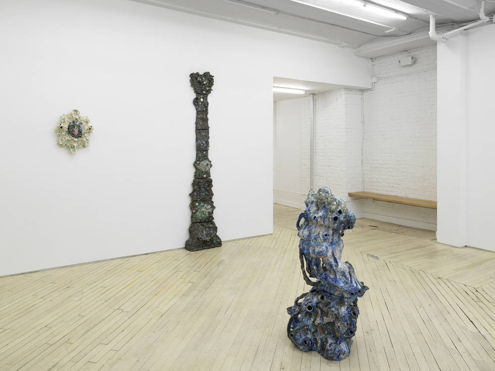A group of abstract ceramic sculptures installed on the floor and walls of a large gallery. 