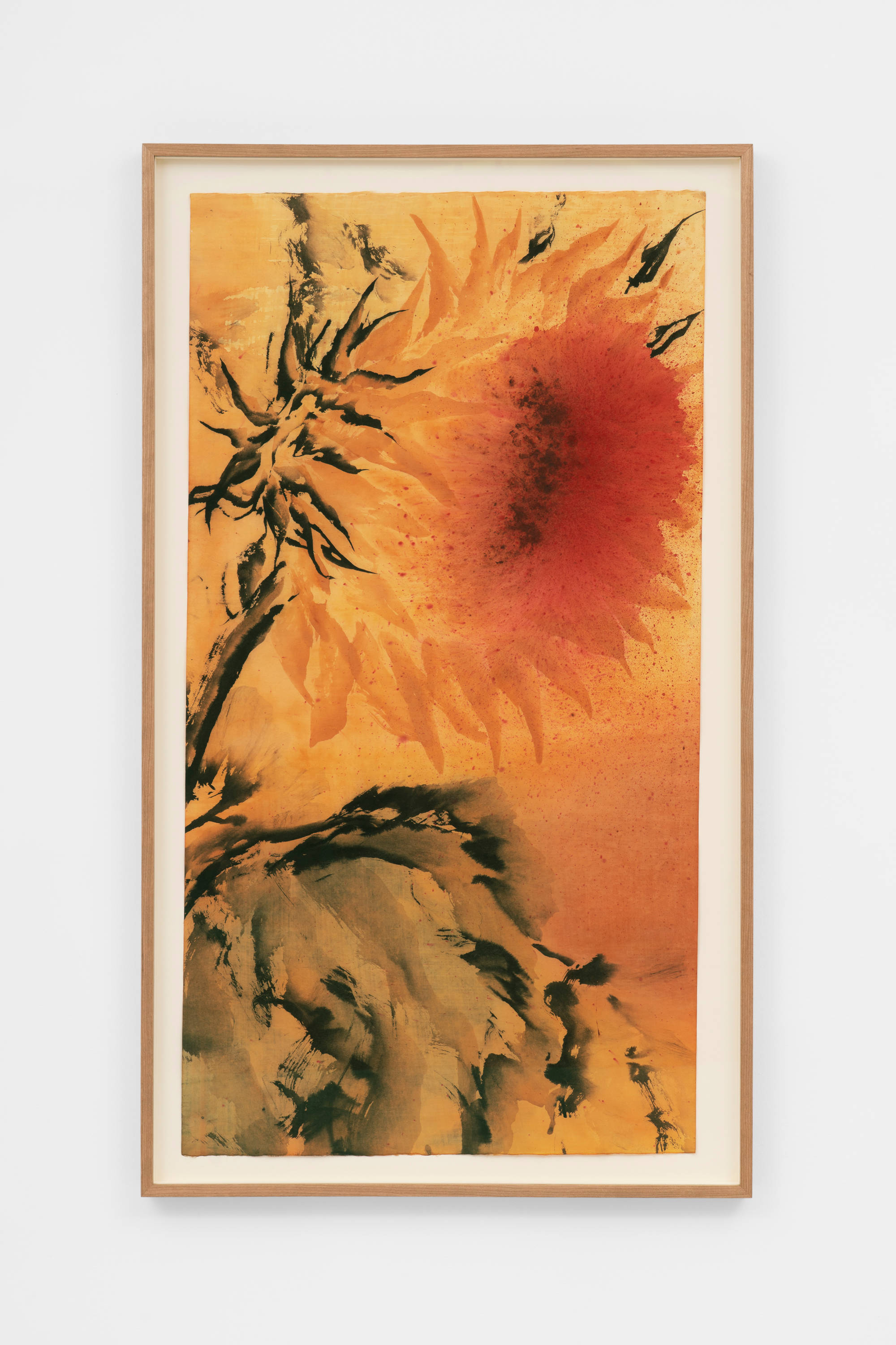 An ink painting of an orange-ochre sunflower with its head facing right, with a black stems and black leaves. The center of the sunflower is executed as a diffuse reddish mass. The sunflower is set against a background of a similar coloration as its petals, and the black leaves take up most of the bottom half of the composition. The frame and the wall the work is mounted on is visible in the shot.
