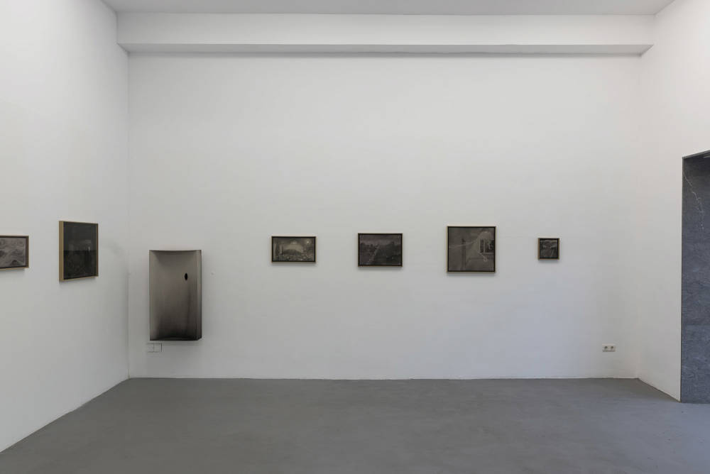 Several framed charcoal drawings in a gallery space with a large window.