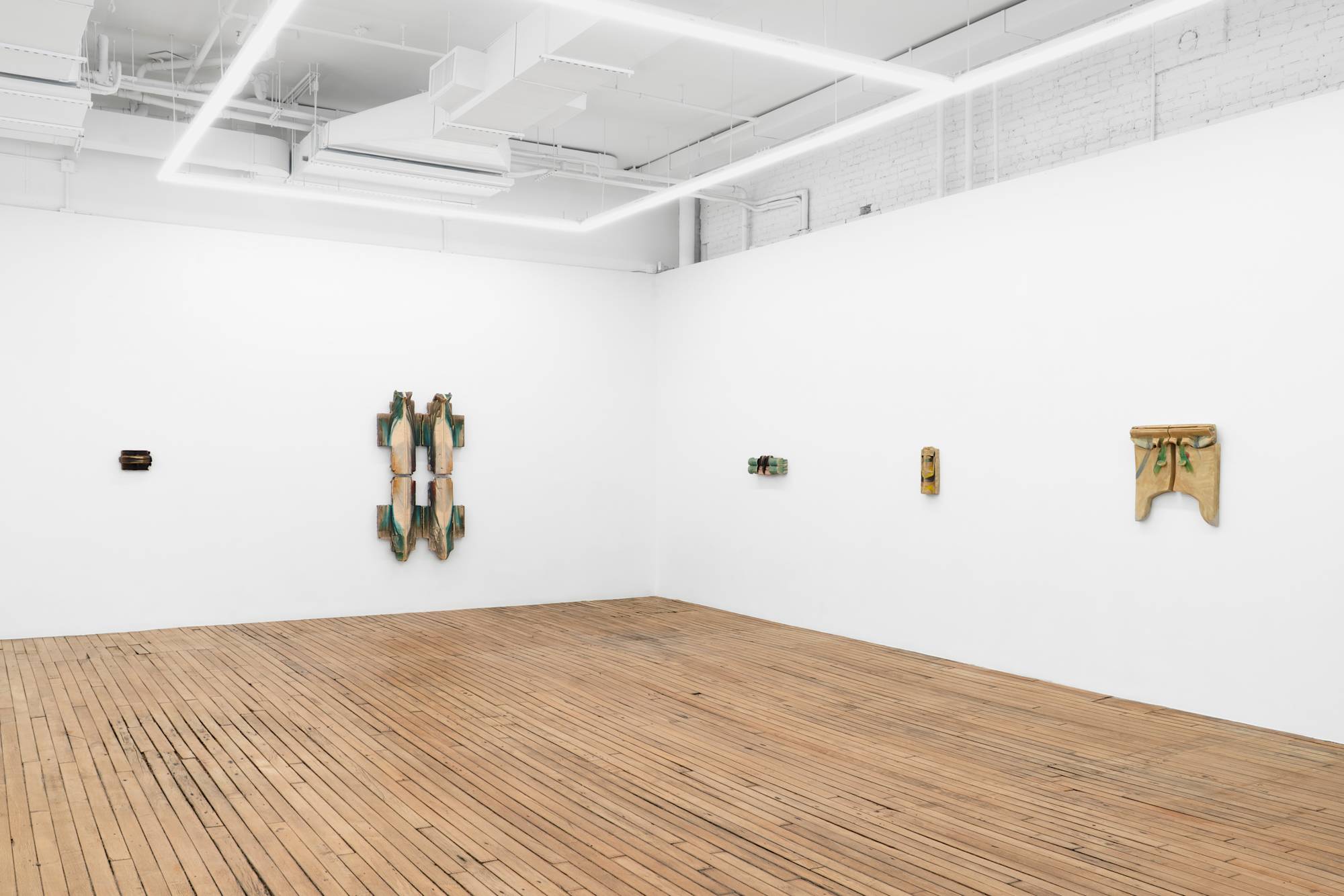 Five wall-mounted ceramic sculptures of various color and scale hang in the corner of a well lit art gallery with white walls and wooden floor.