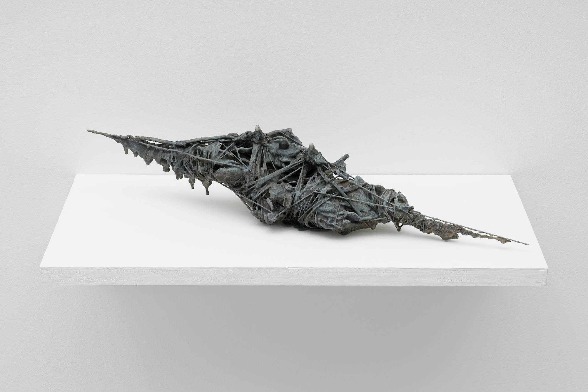 A grey, abstract sculpture by Matt Hoyt sits on a white shelf. The sculpture is highly textured and wiry. It appears to have been wrapped in some material many times over.