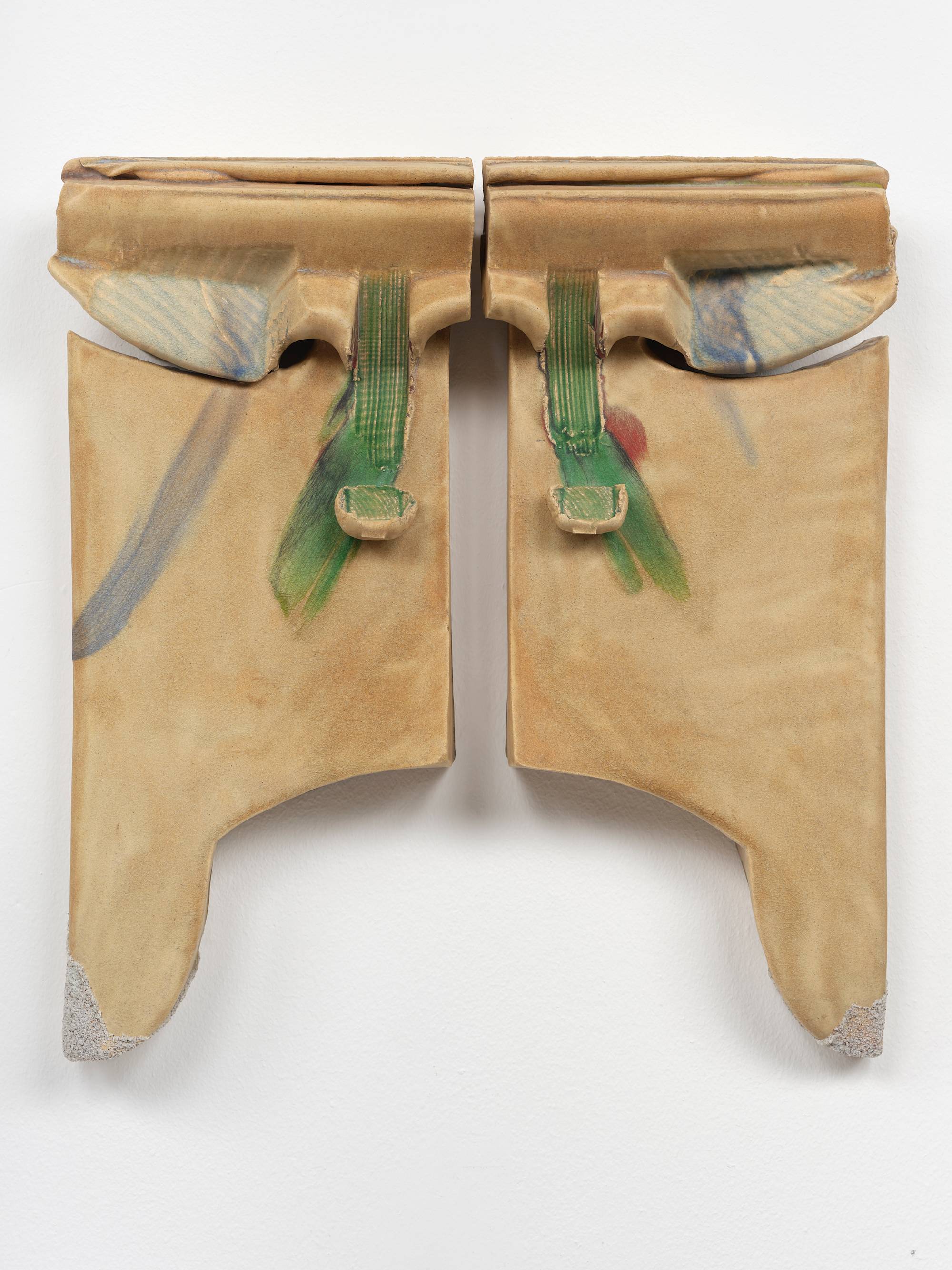 Two ceramic sculptures hang on a wall mirroring each other with a thin channel dividing them. The clay has been pushed and stamped to create appendages near the upper edges that resemble small wings glazed faintly blue. Towards the center of the composition, both pieces have been gouged in a downward motion through the shoulder of the wings resulting in narrow vertical troughs that end in a small lifted flaps. A green glaze runs through the troughs and flaps. Each sculpture is tipped with a small peninsula still coated with sand from the kiln they were fired in.