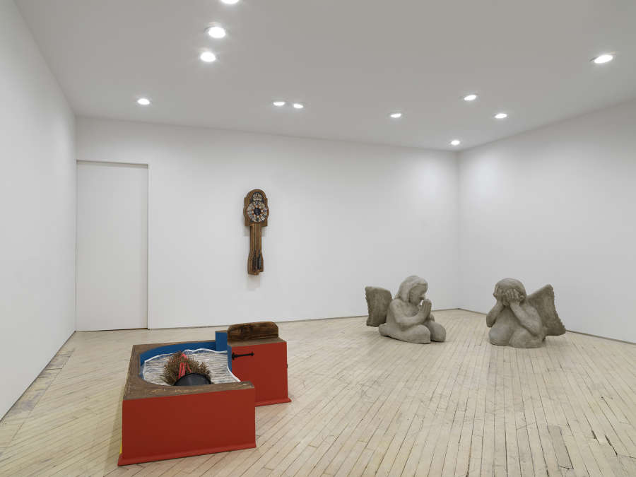 Image of a solo exhibition by Libby Rothfeld showing a number of sculptures on the ground and a painting of a clock hanging on the rear wall. 