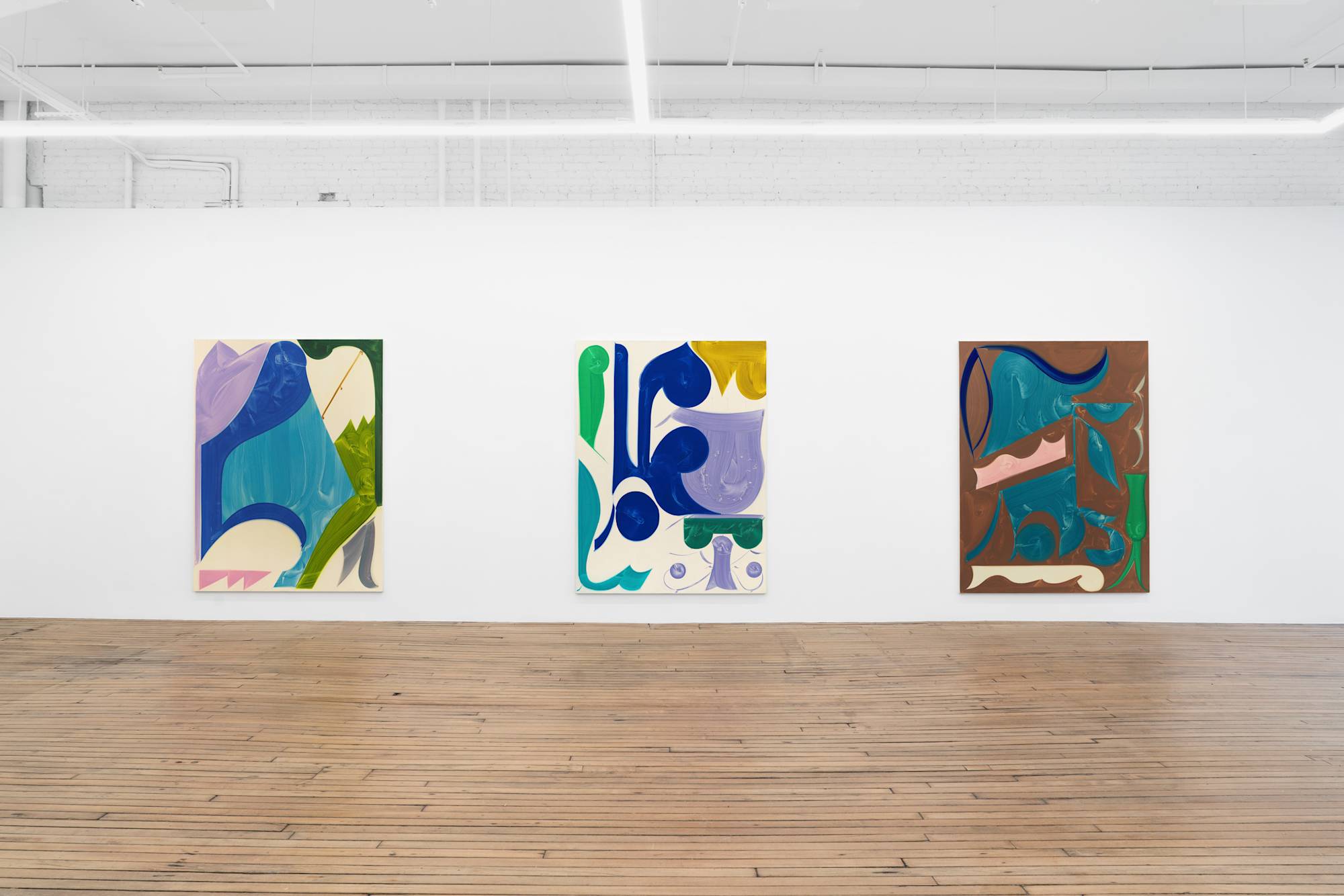 Three abstract paintings of simple shapes and bold colors hang in an art gallery with white walls and wood floor.