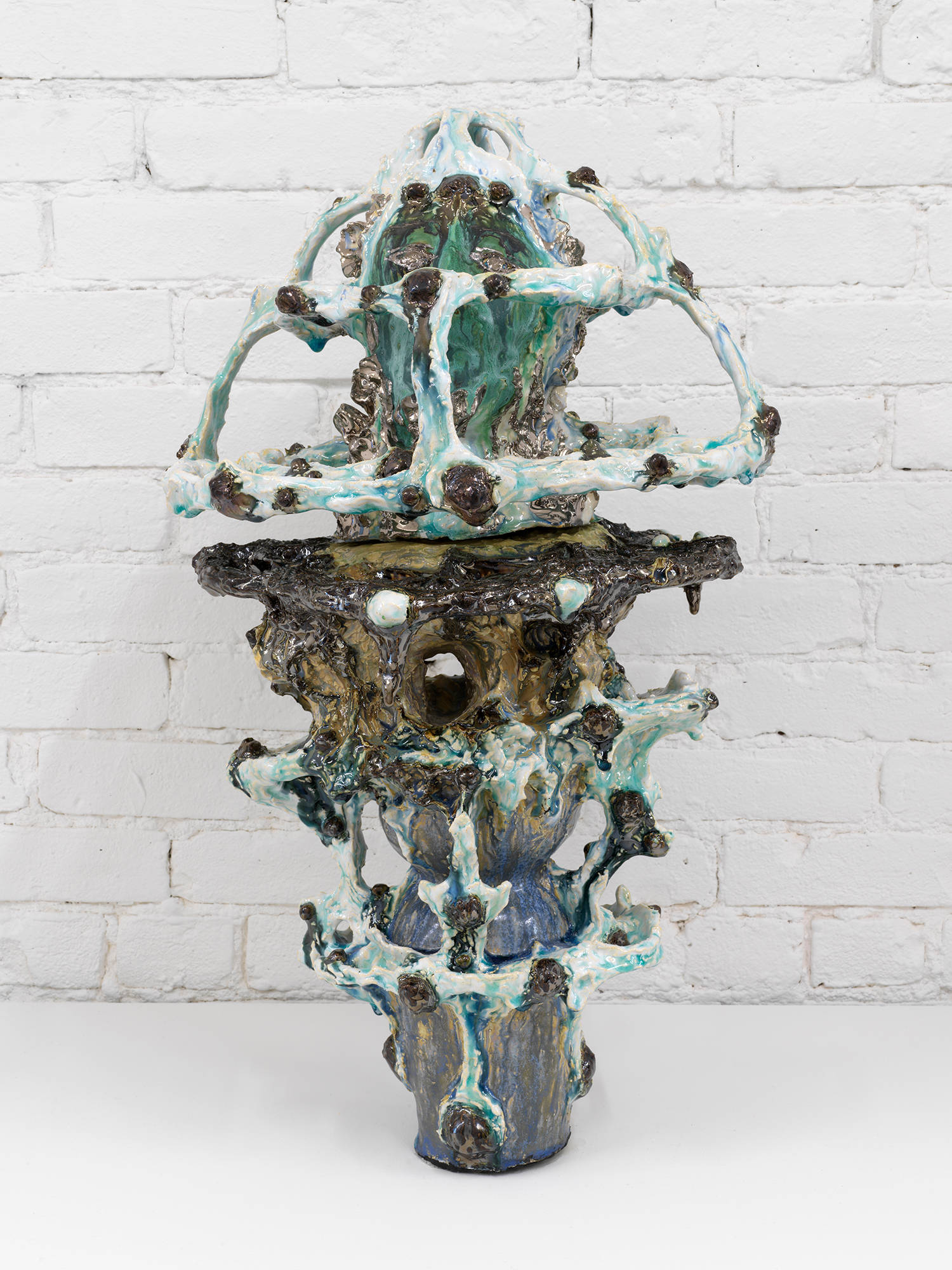 An abstract ceramic sculpture resembling a vessel installed in front of a brick wall.