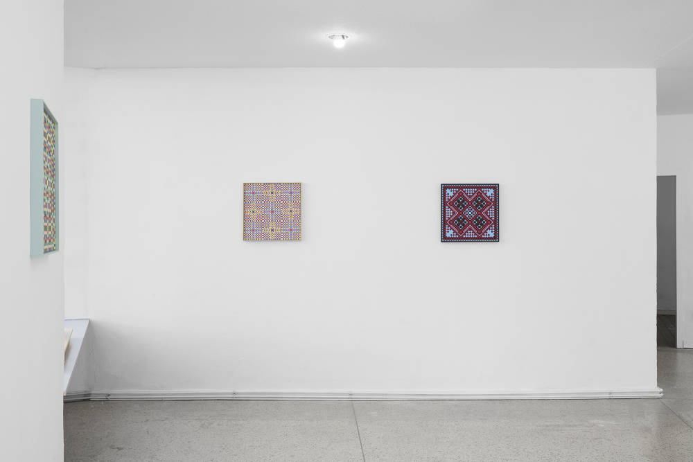 Image of a wall with two colorful grid paintings next to each other. On the left side is another wall with another colorful grid painting. 