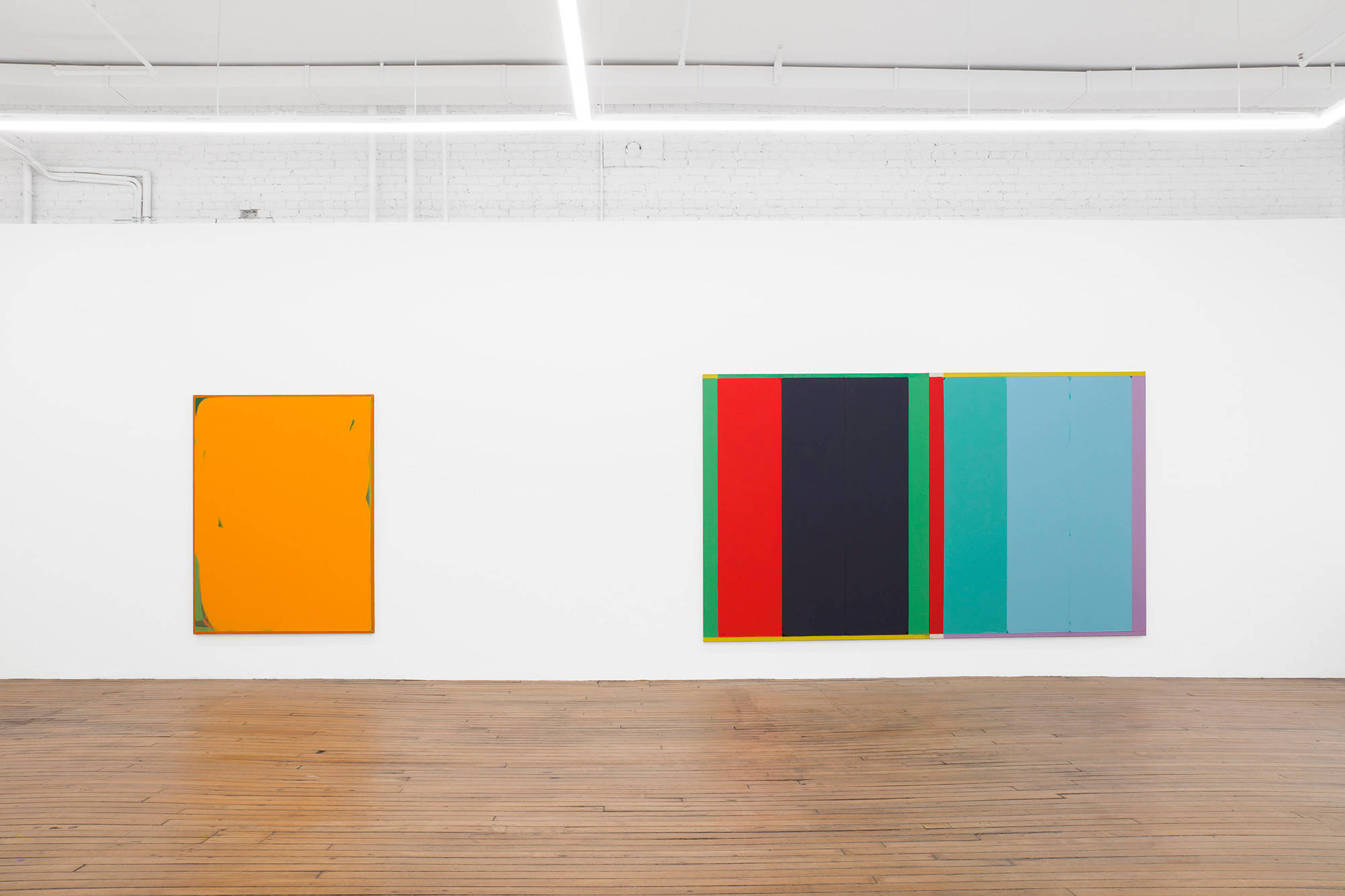 Two large abstract paintings hung on a long gallery wall above a brown wooden floor. The paintings are rendered primarily in orange, red, black, green, and blue.