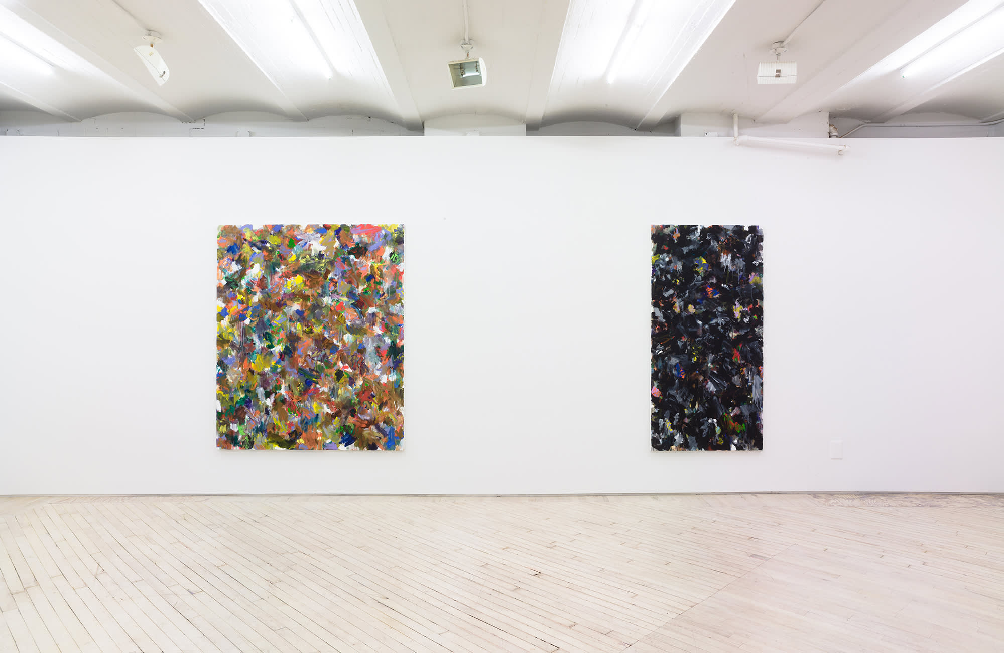 In a gallery space, two large abstract paintings are hung evenly spaced apart on a large white wall. The paintings contain numerous swatches of various colors painted on top of one another. The paint is thin and in some areas dripping.