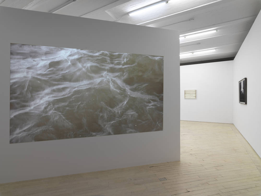 In a corner of a gallery space, a large digital projection of moving water.