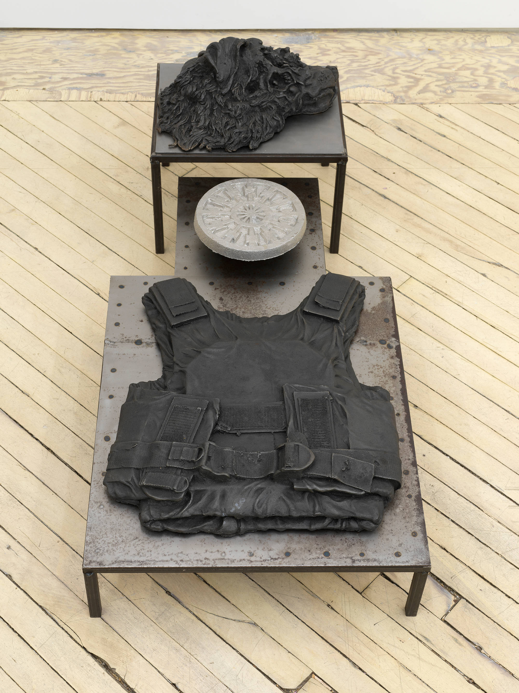 In a gallery space, an iron sculpture depicting abstracted forms on top of a plinth.