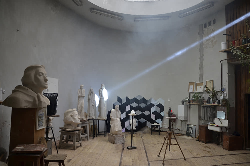 Inside a round room classical figurative sculpture lines the walls. A single ray of sunshine beams across the image and illuminates one of the sculptures. 