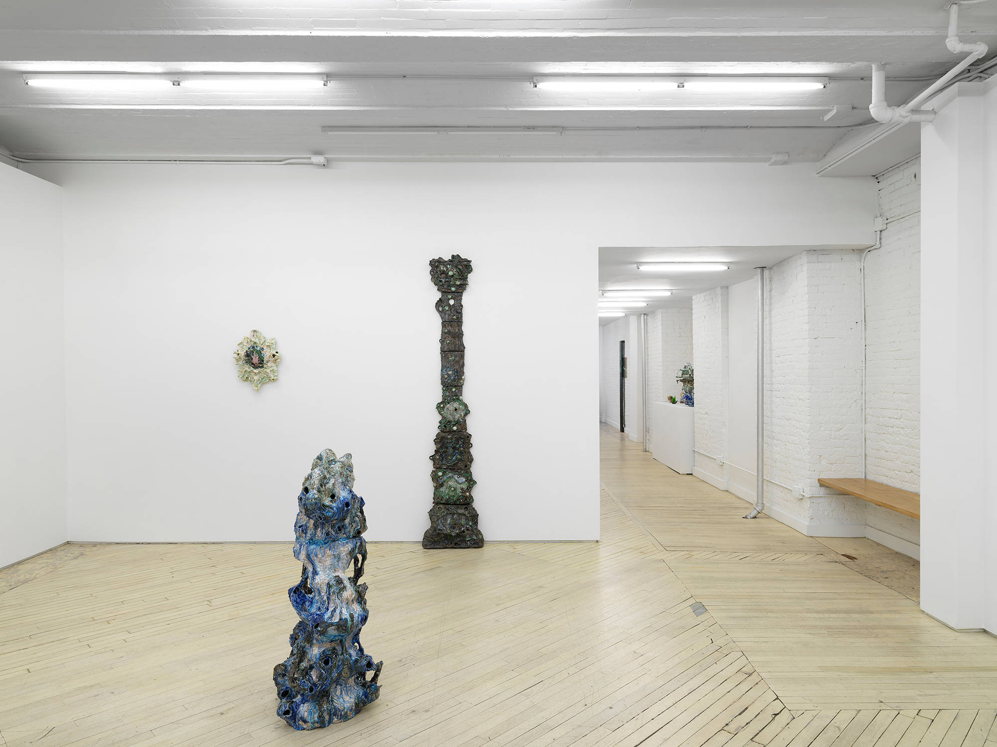 A group of abstract ceramic sculptures installed on the floor and walls of a large gallery.