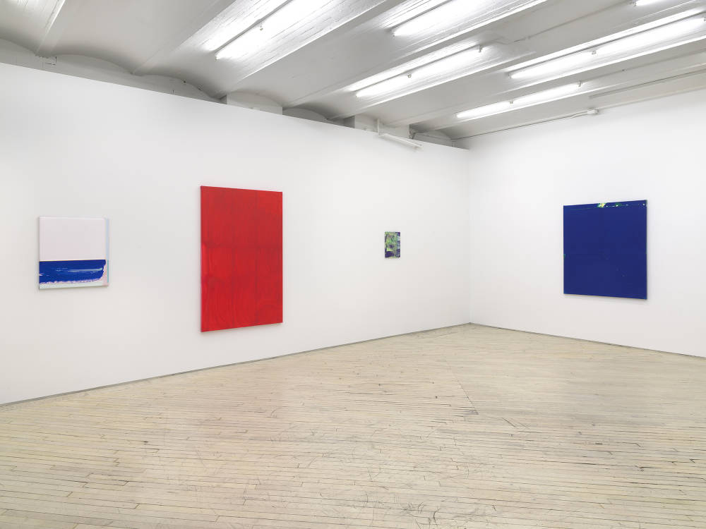 Four abstract paintings in a gallery space. To the left a small blue and white square painting. To its right is a larger red monochrome painting with a brushy surface. On the right wall is a large blue monochrome painting. In the center of the larger works is a small brushy green and purple painting.